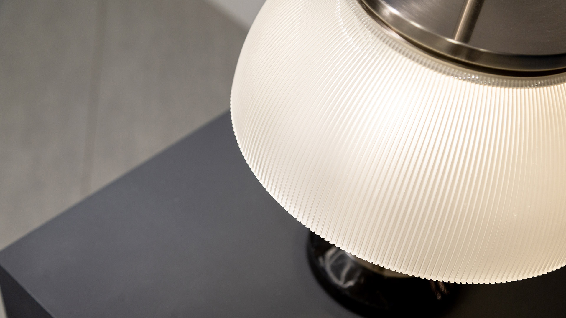 Lampada da tavolo Artemide Alfa con diffusore a cupola, stelo nero e terminale sferico, mostrata in due varianti colore su sfondo rosso