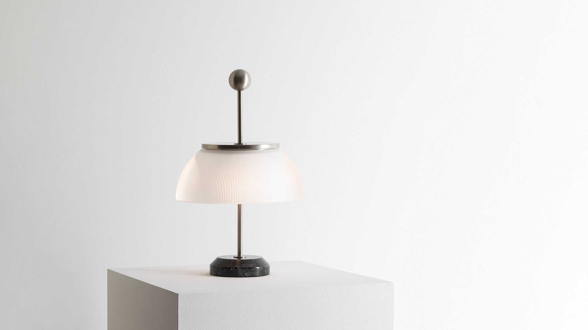Lampada da tavolo Artemide Alfa con diffusore a cupola bianca e stelo metallico su una scrivania con libri, una statuetta di cavallo e opere incorniciate.