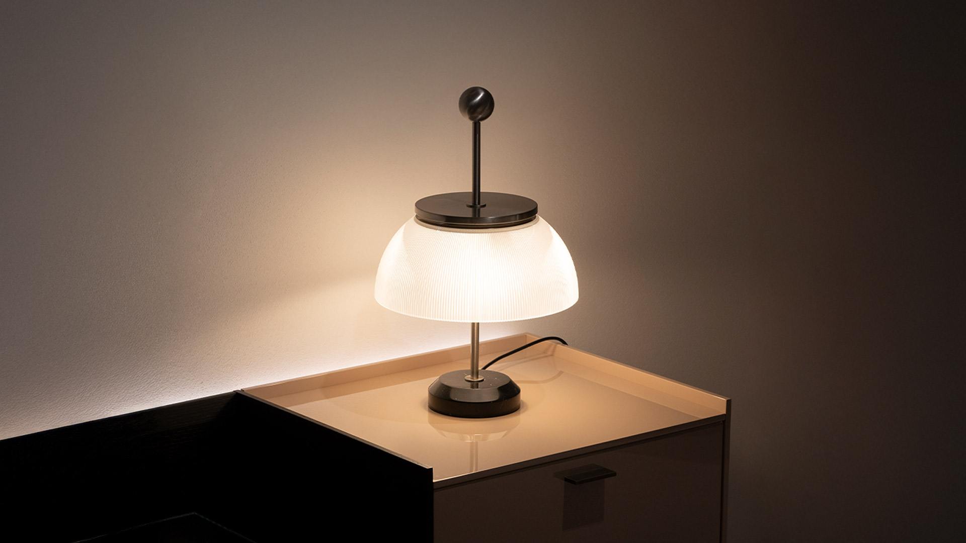 Lampada da tavolo Artemide Alfa con paralume a cupola in vetro opalino nervato e dettaglio superiore in metallo lucido su base scura