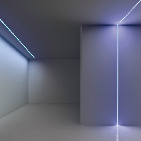 Stanza bianca minimalista con luci LED lineari Artemide Algoritmo System che tracciano i bordi del soffitto e un angolo verticale, emettendo luce bianco-blu fredda