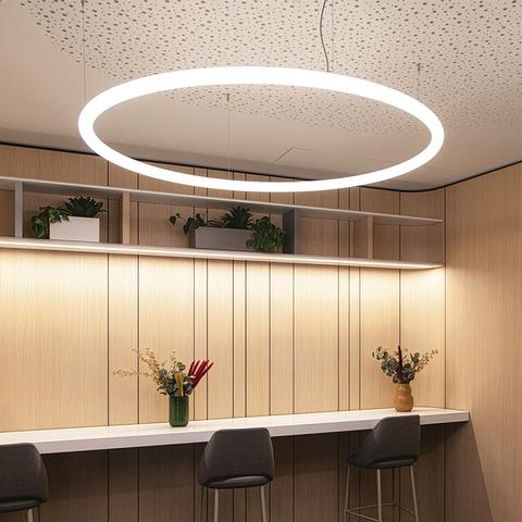 Artemide Alphabet of Light Circular pendant, large white LED ring suspended over a modern wood-paneled bar counter with stools.