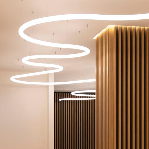 Artemide Alphabet of Light System: spiral pendant installation with luminous white circular rings suspended from ceiling near wooden slat wall