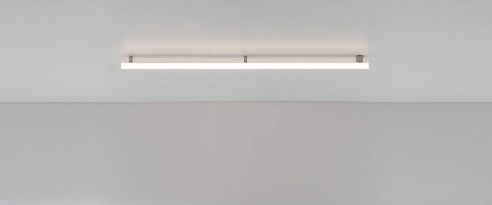 Ufficio moderno con postazioni aperte e una sala riunioni in vetro con lampade Artemide Alphabet of Light Linear su pareti gialle.