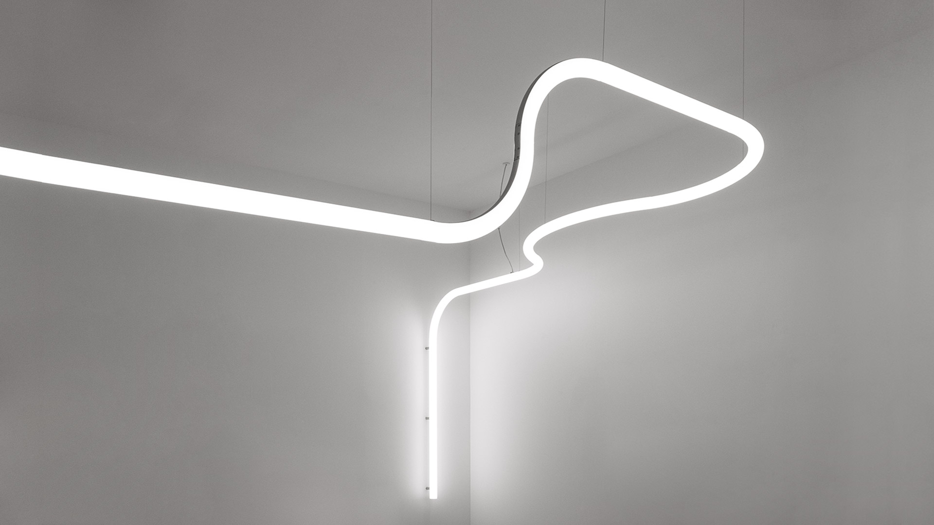 Artemide Alphabet of Light System: tubi LED bianchi luminosi che formano figure sulla parete, con due lampade da tavolo circolari nere su piedistallo bianco