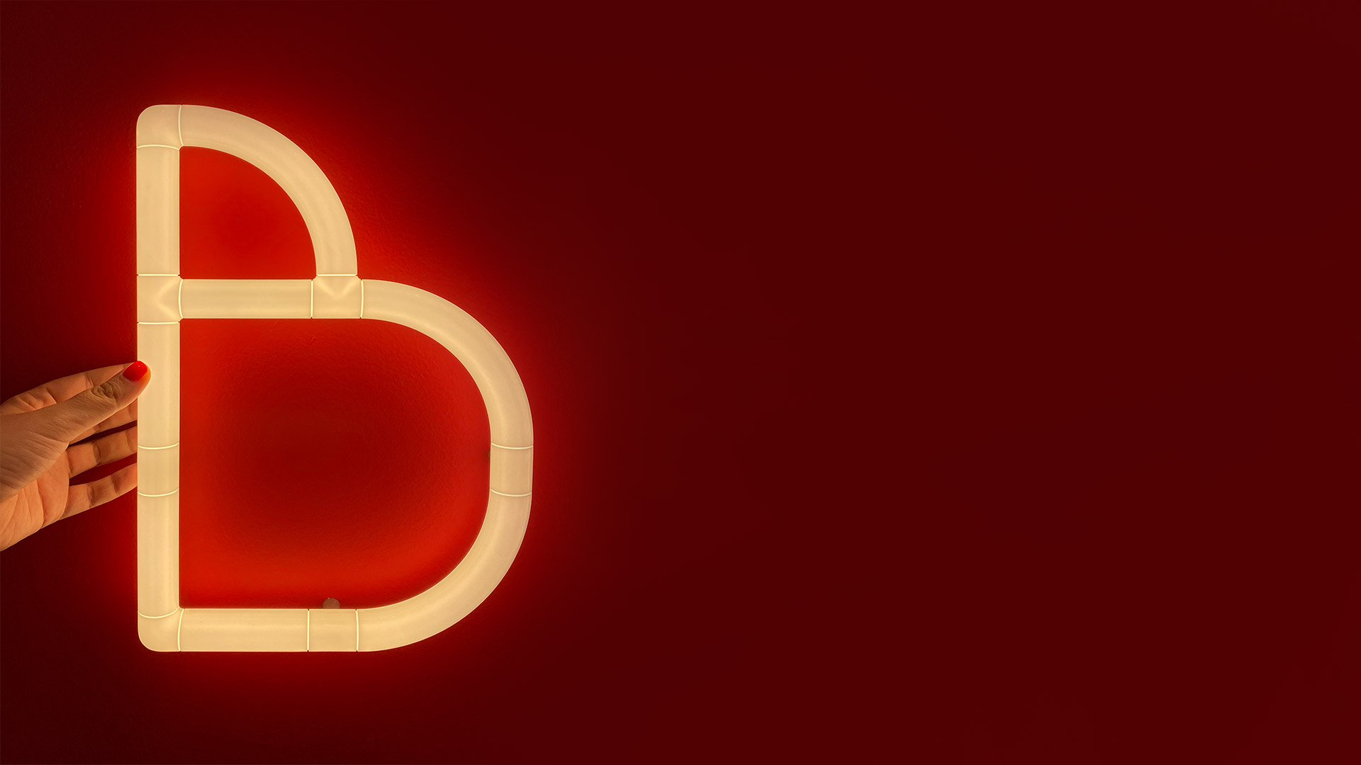 Lettere luminose 'BIG' in stile neon di Artemide Alphabet of Light Mini su parete rossa, accanto a un tavolino con piante in vaso