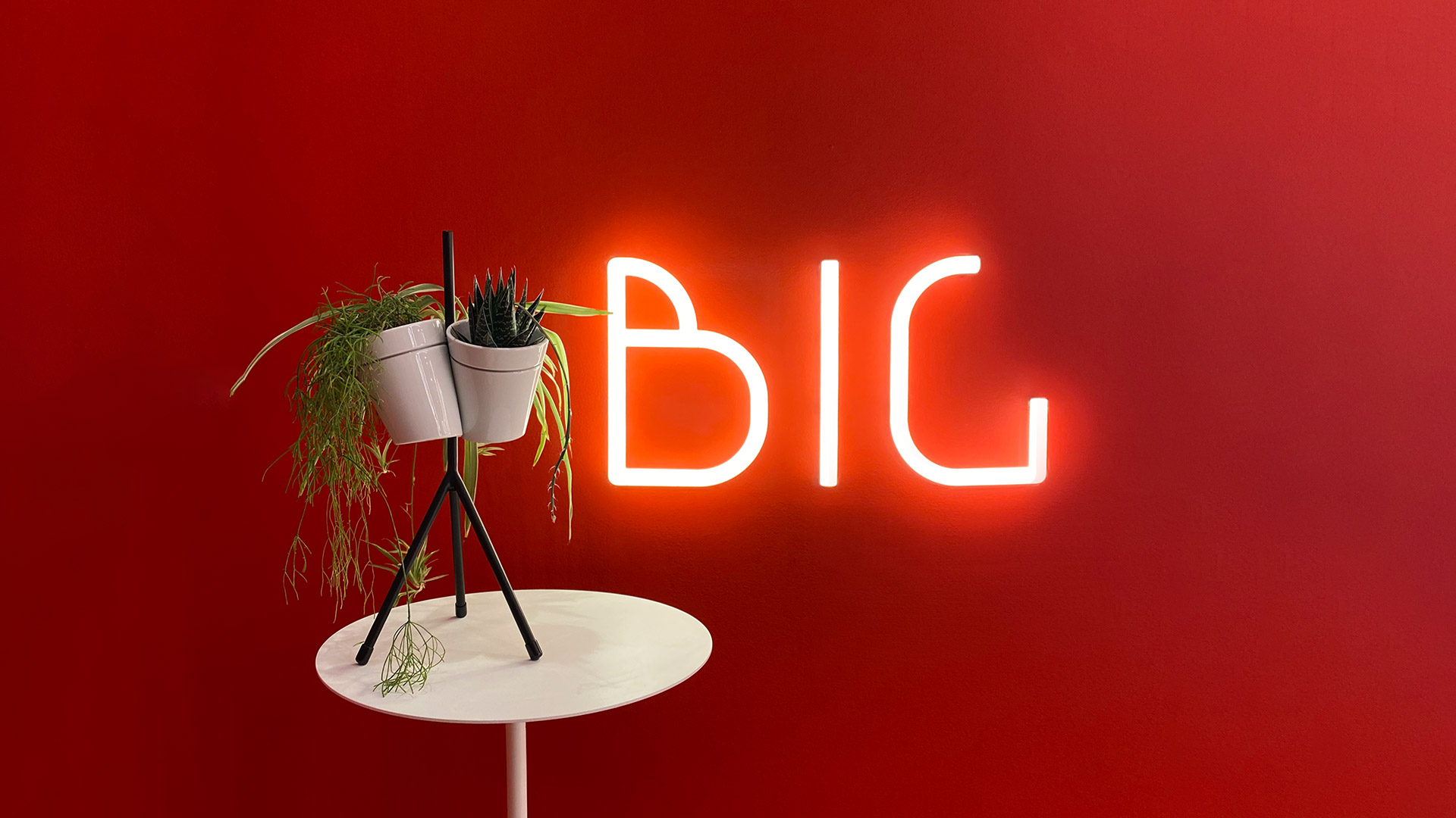 Mano che regge la lettera B luminosa di Artemide Alphabet of Light Mini, illuminazione rossa calda su sfondo rosso scuro