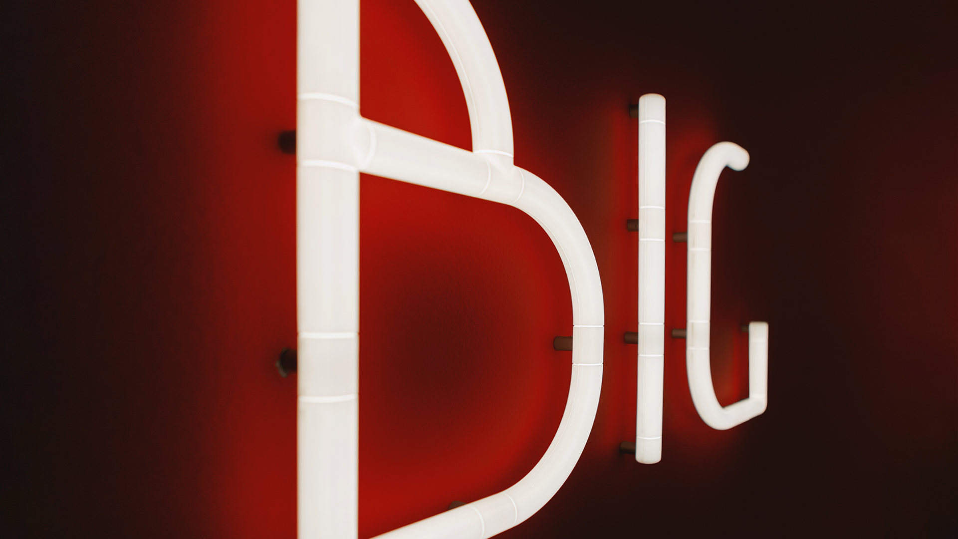 Lettere luminose in stile neon bianco che formano 'BIG' montate su parete rossa, dalla collezione Artemide Alphabet of Light Mini