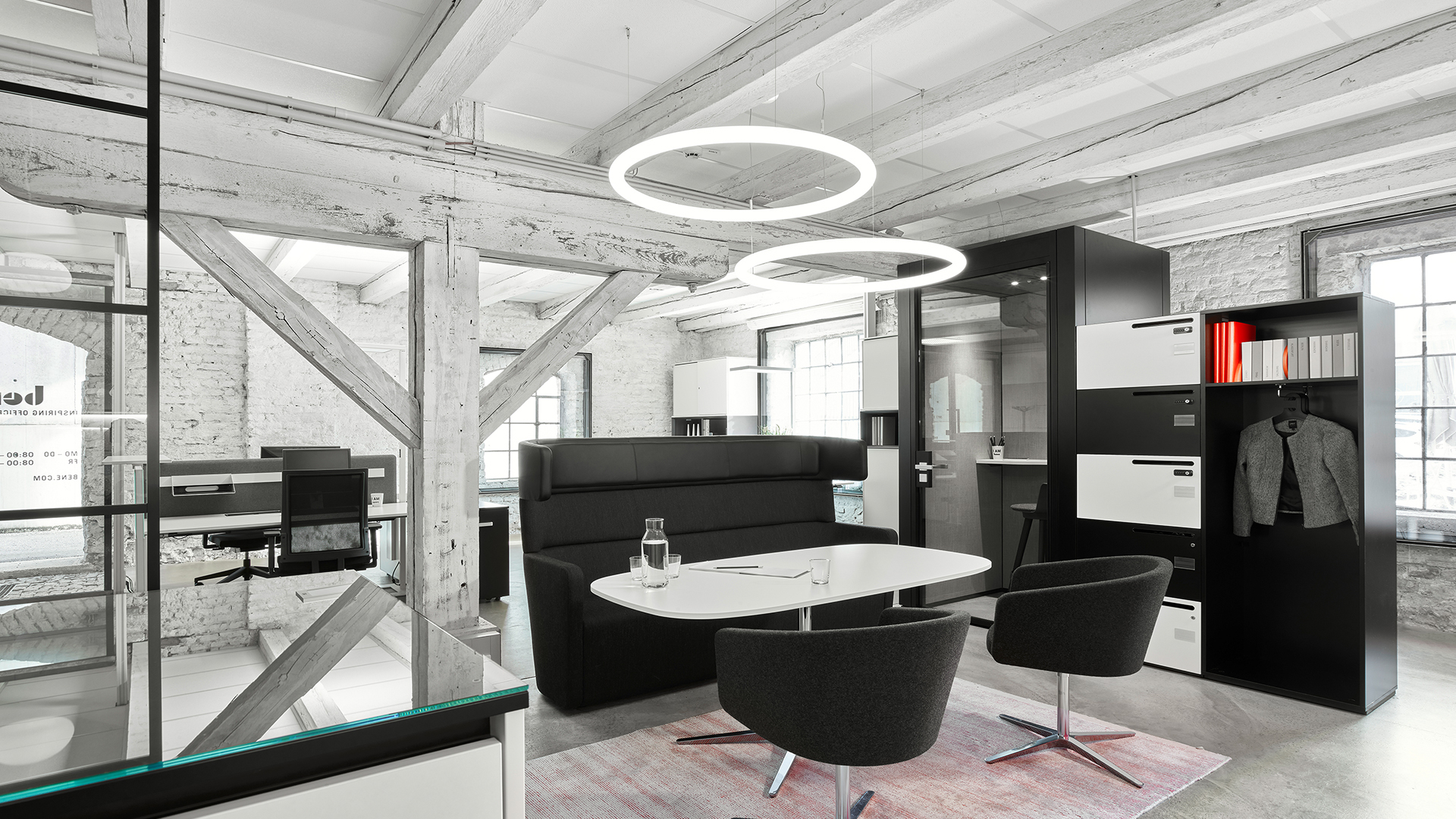 Tre lampade a sospensione Artemide Alphabet of Light Circular di diverse dimensioni appese a un soffitto industriale sopra una parete decorata.