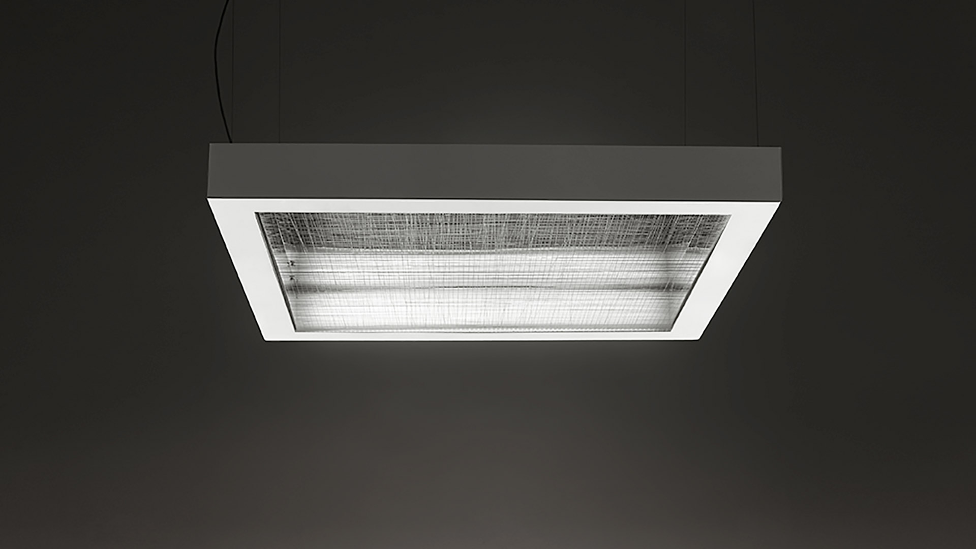 Lampada a sospensione Artemide Altrove: struttura rettangolare in metallo grigio con bordo interno bianco e diffusore in vetro texturizzato, sospesa a cavo