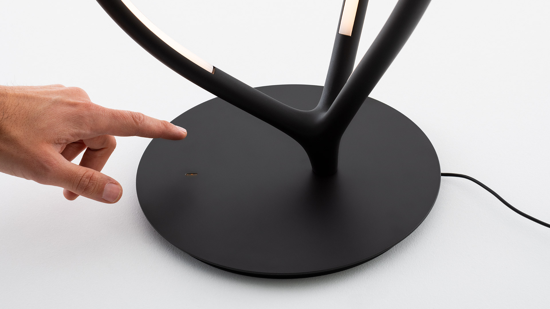 Due lampade da tavolo Artemide Arrival: sinistra struttura a goccia dorata, destra struttura nera con striscia LED integrata, su basi circolari