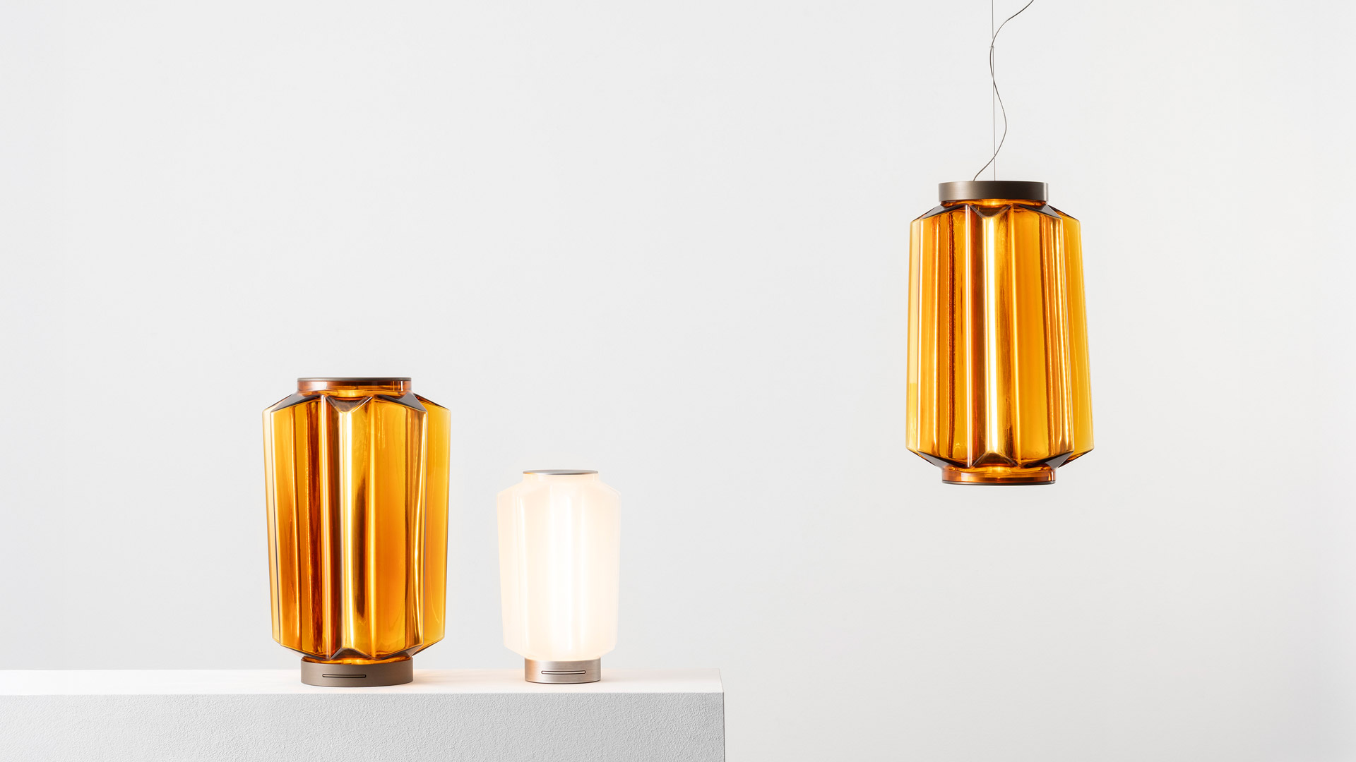 Lampada da tavolo Artemide Auralia in vetro ambra con corpo geometrico sfaccettato, luminosa e calda su un tavolo in legno accanto a una piccola scultura lignea