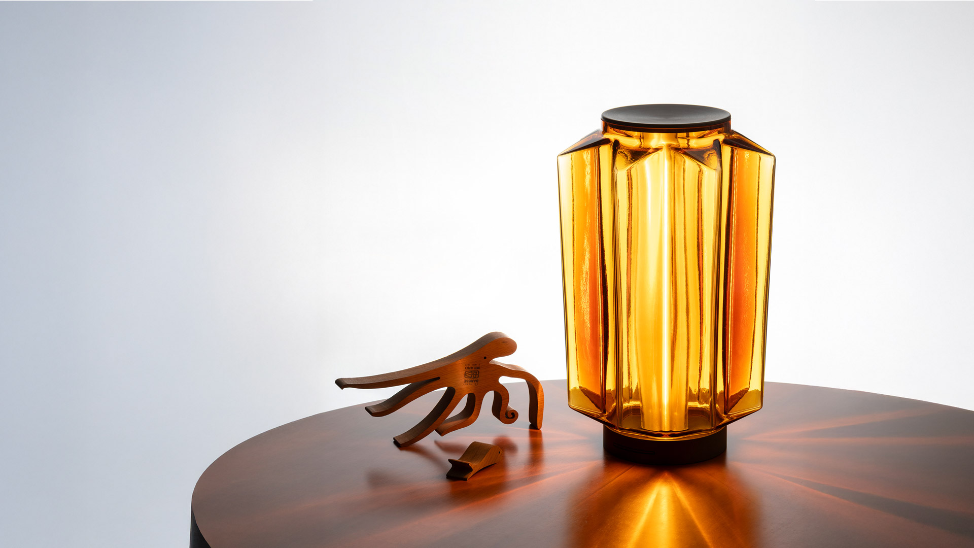 Lampade Artemide Auralia: due lampade da tavolo in vetro ambra e una a sospensione, con paralumi cilindrici sfaccettati e calda luce dorata