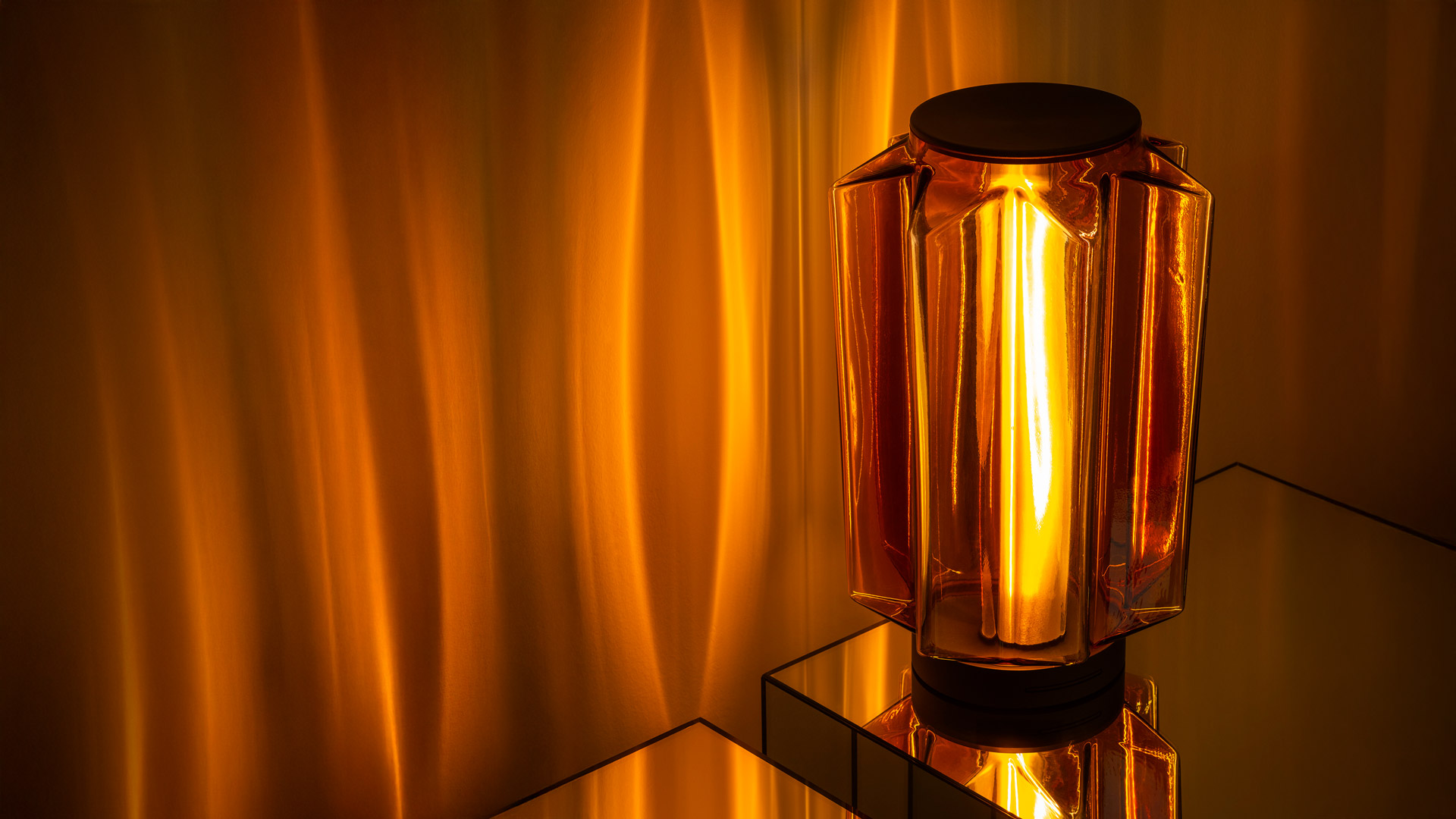 Lampada da tavolo Auralia di Artemide: diffusore geometrico in vetro ambra con bulbo a filamento a vista che proietta calda luce dorata sulle superfici circostanti