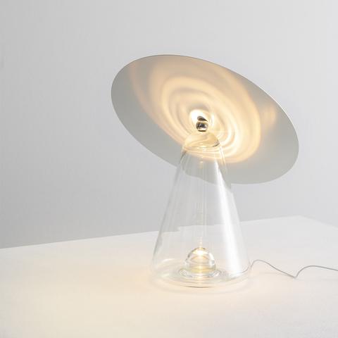 Lampada da tavolo Artemide Boltons: base a cono in vetro trasparente con paralume a disco cromato inclinato verso l'alto, proietta motivo luminoso a spirale