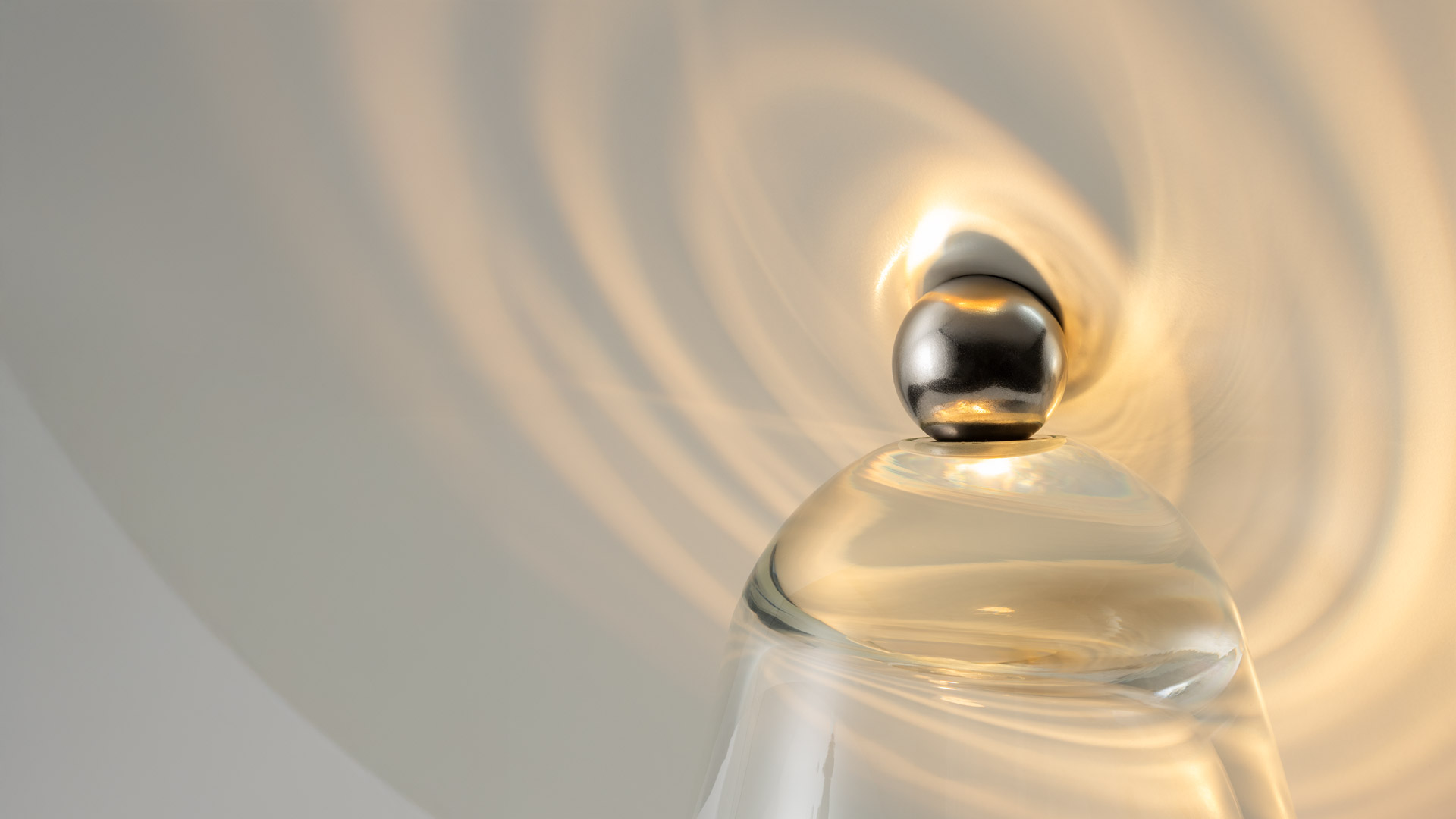 Lampada da tavolo Artemide con riflettore a disco dorato inclinato su base conica in vetro trasparente, che proietta luce spirale calda su una superficie in marmo.