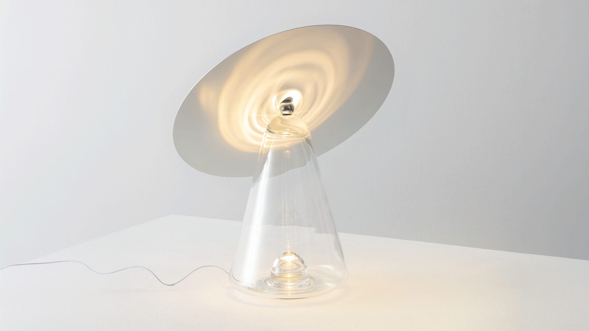 Lampada da tavolo Boltons con paralume conico in vetro e luce calda su una credenza in legno, accanto a una poltrona in pelle su parete blu intenso