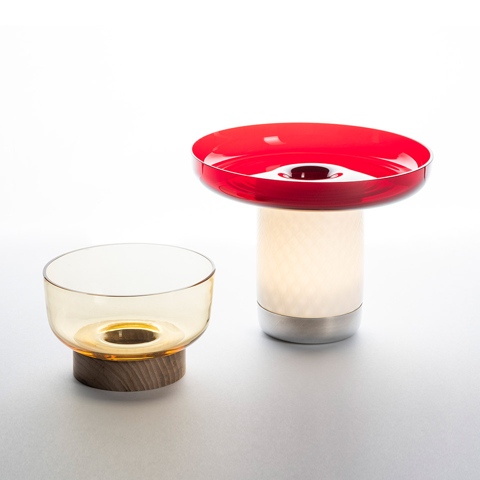 Two Artemide Bontà table lamps: left amber glass bowl on wood base, right illuminated white cylinder with red disc top