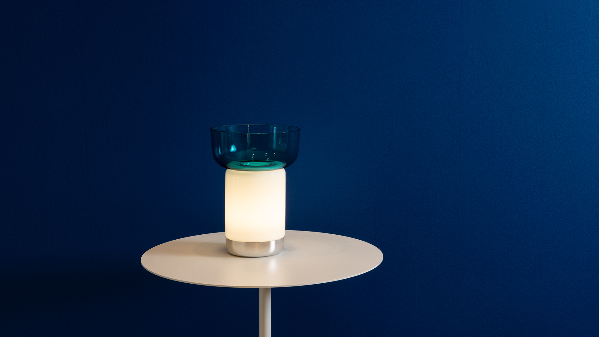 Close-up of Artemide Bontà lamp base: polished chrome curved base supporting a white textured glass shade with diamond pattern