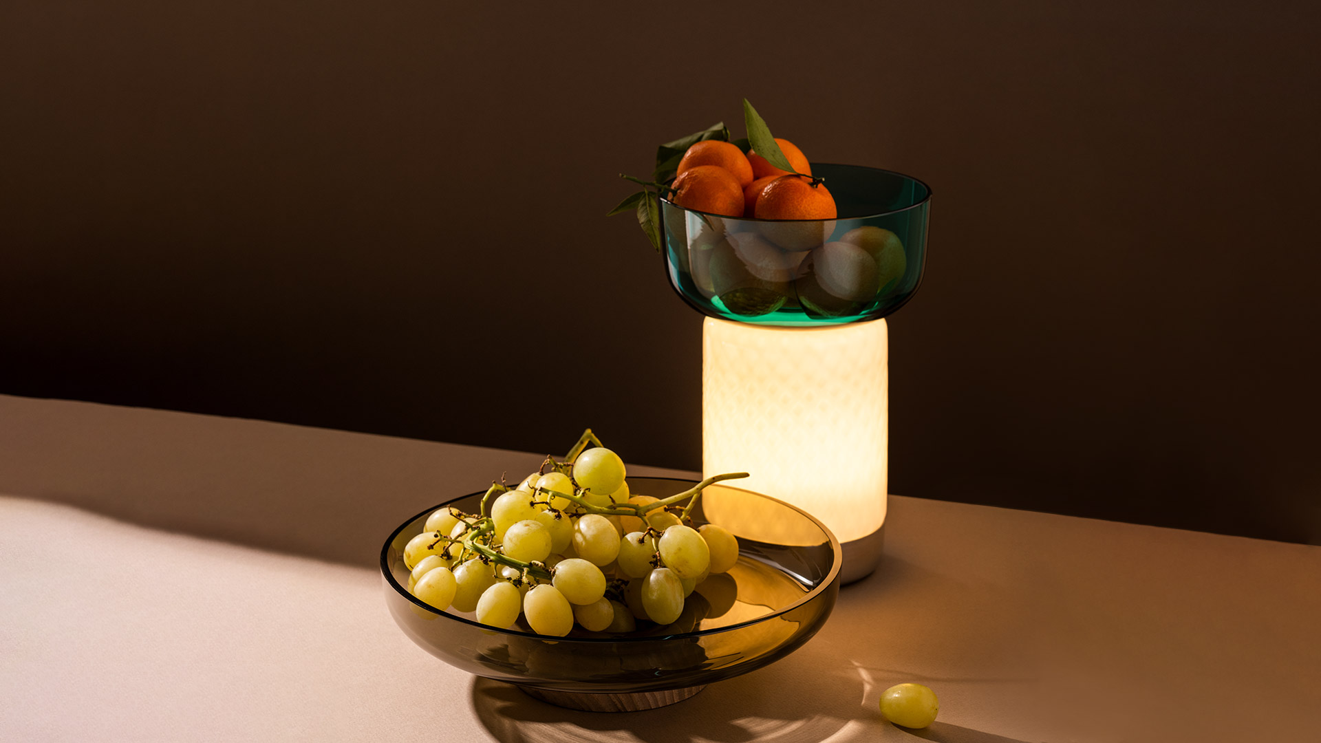 Artemide Bontà table lamp with glowing white opal cylinder base and teal blown glass bowl on top, placed on a white side table