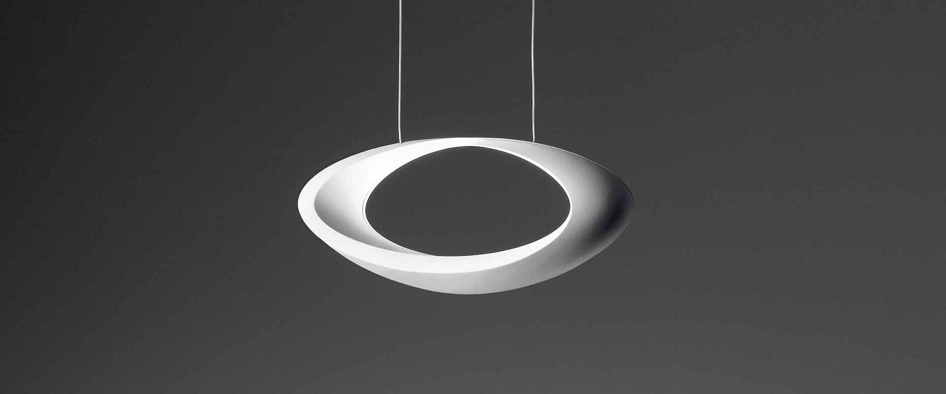 Woman reaching up toward Artemide Cabildo pendant lamp, a glowing circular LED ring suspended in darkness