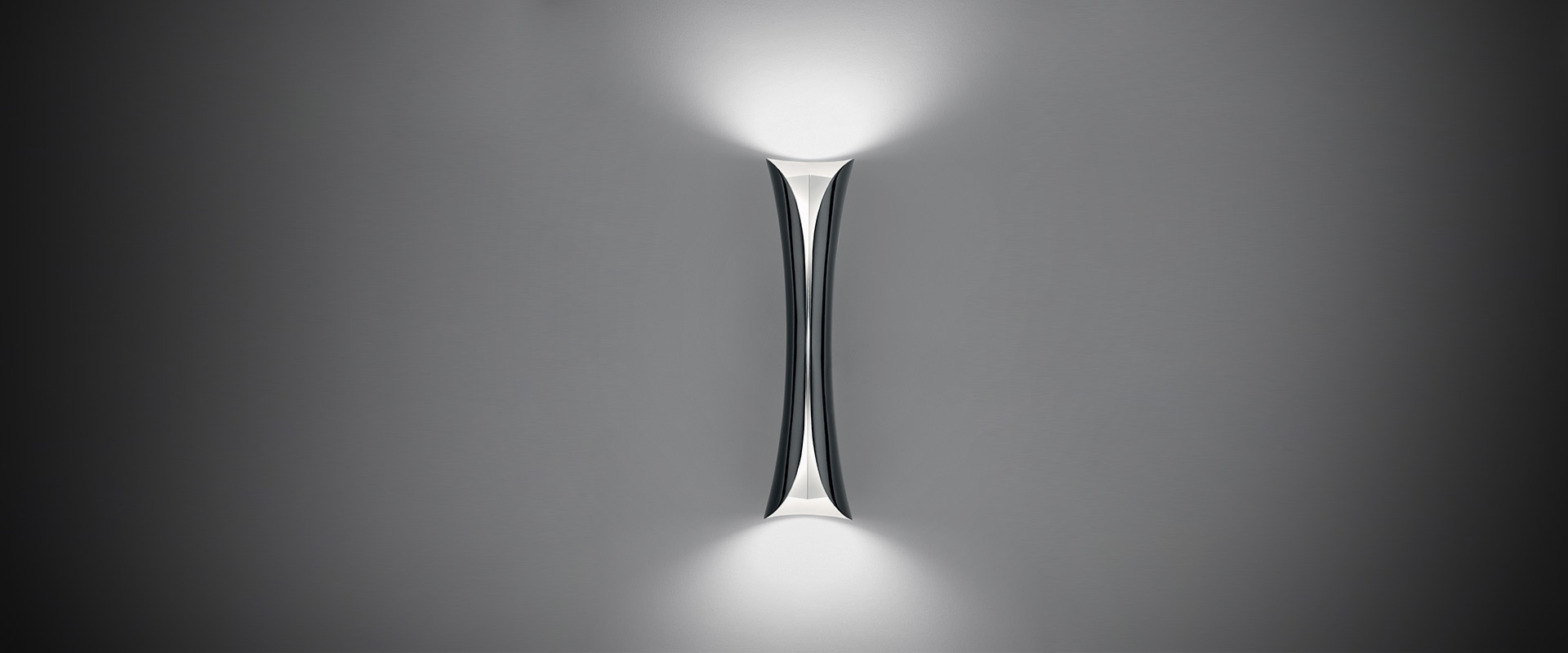Artemide Cadmo floor lamp with sleek twisted metallic column body emitting upward light, displayed on a white pedestal
