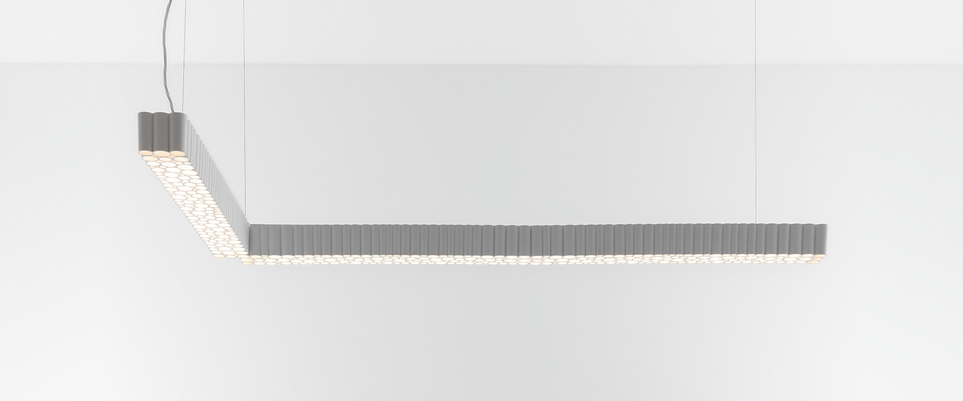 Artemide Calipso Linear System: lampada a sospensione ad L in grigio con diffusori LED circolari che creano un motivo a nido d'ape, appesa al soffitto