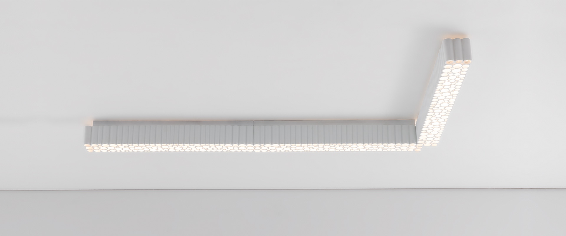 Artemide Calipso Linear System: plafoniera a soffitto a forma di L con pannello diffusore LED strutturato in bianco, montata a filo del soffitto