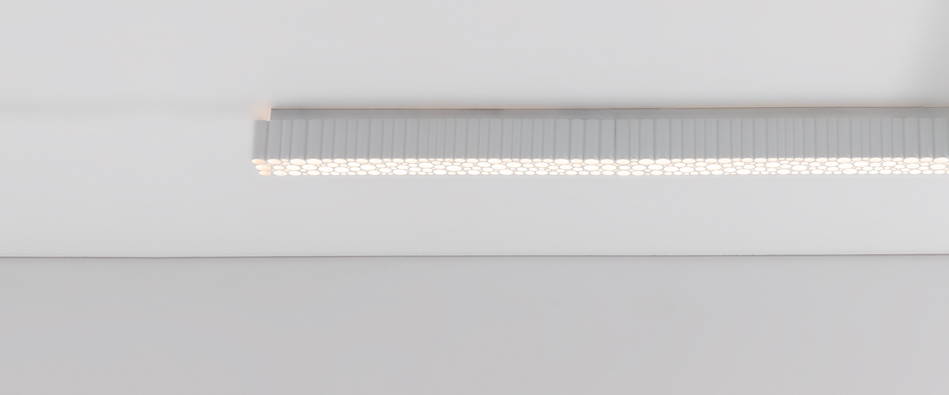 Lampada a sospensione Artemide Calipso Linear Stand Alone bianca sopra un tavolo da pranzo con vasi e mele verdi