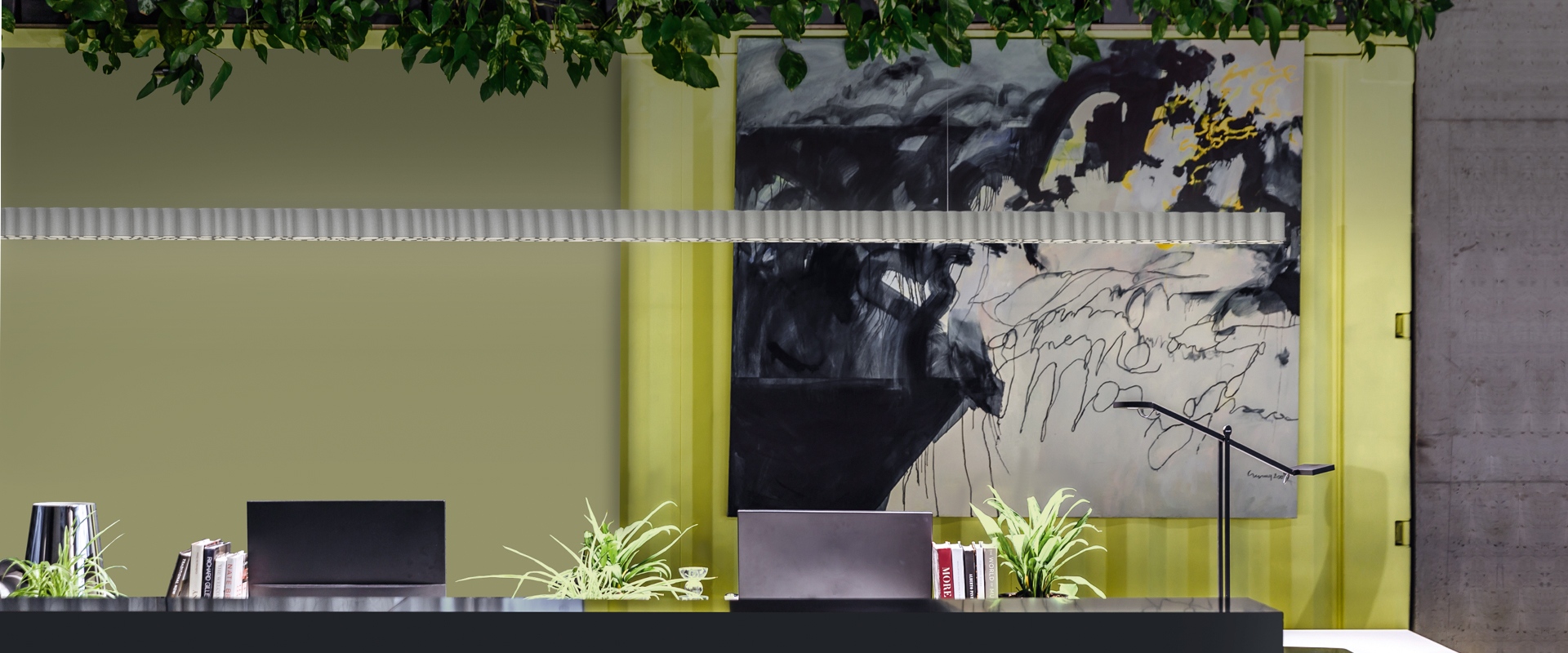 Reception moderna con lampada a soffitto Artemide Calipso Linear System, piante verdi, opera d'arte astratta e accenti gialli su pareti verde salvia