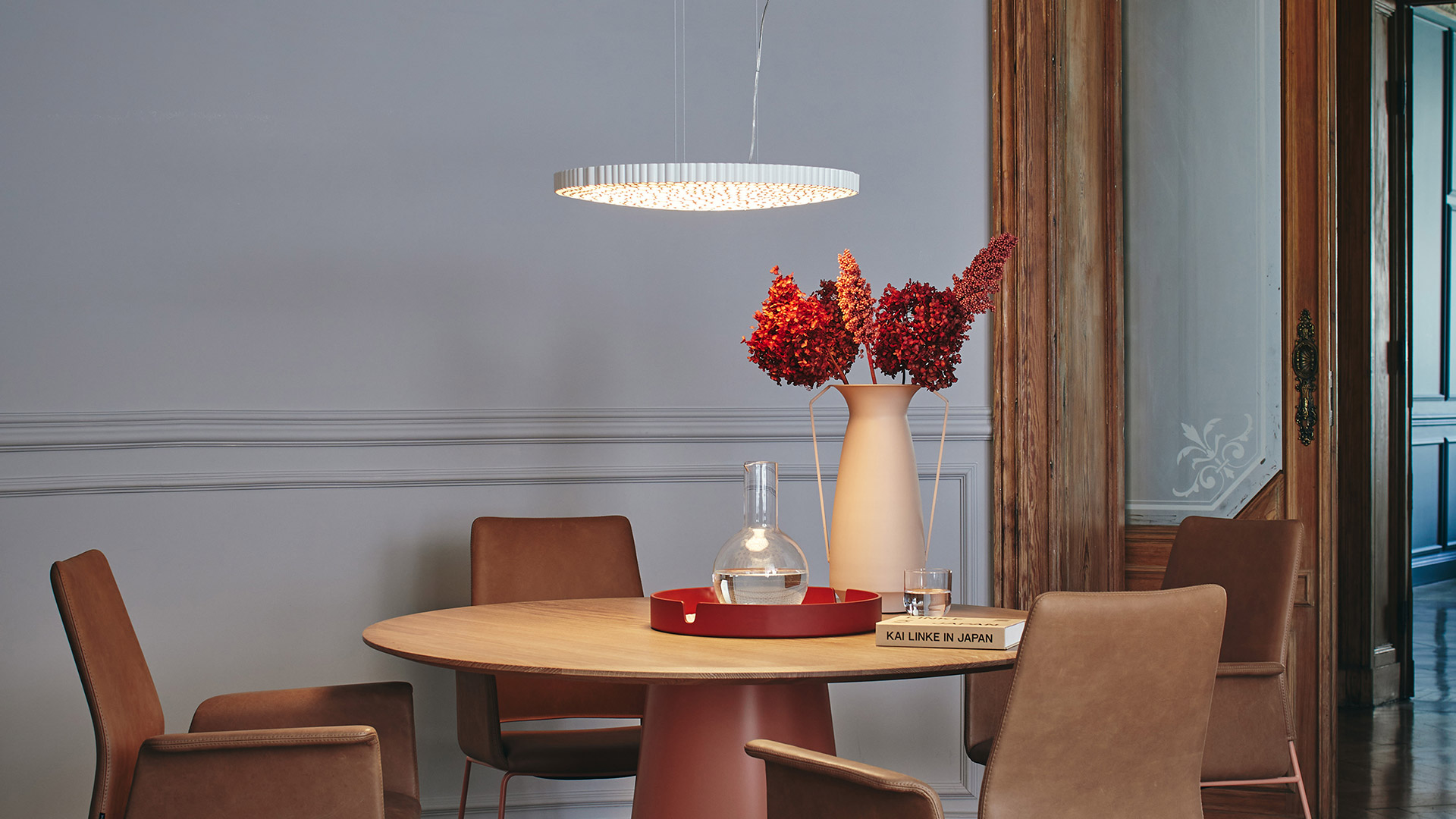 Lampada a sospensione Calipso di Artemide, anello LED circolare con bacchette di cristallo, sopra un tavolo rotondo con sedie e composizione floreale