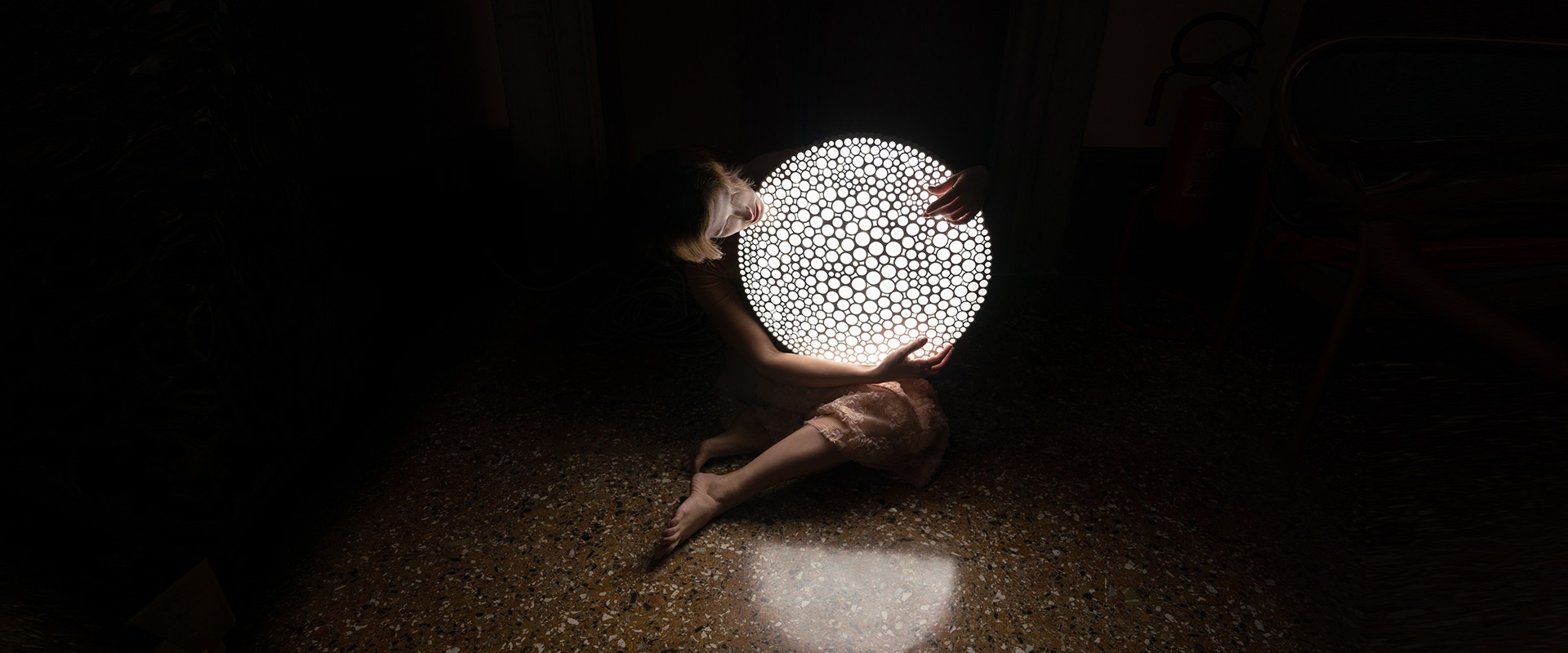 Persona che tiene tra le braccia la lampada sferica Artemide Calipso con motivo perforato organico, che proietta luce su un pavimento scuro