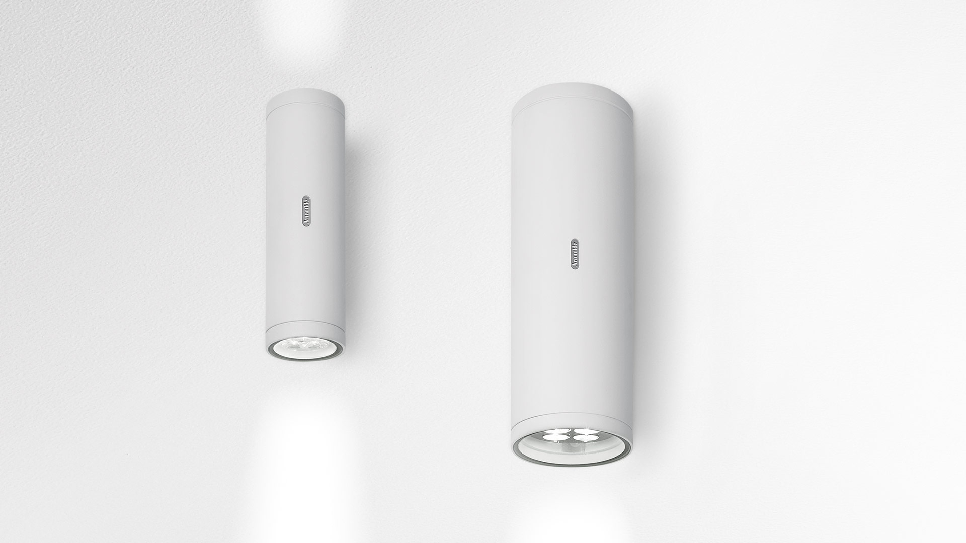 Two Artemide Calumet wall lights in white, cylindrical shape, downward LED beam, shown in two sizes on a white wall