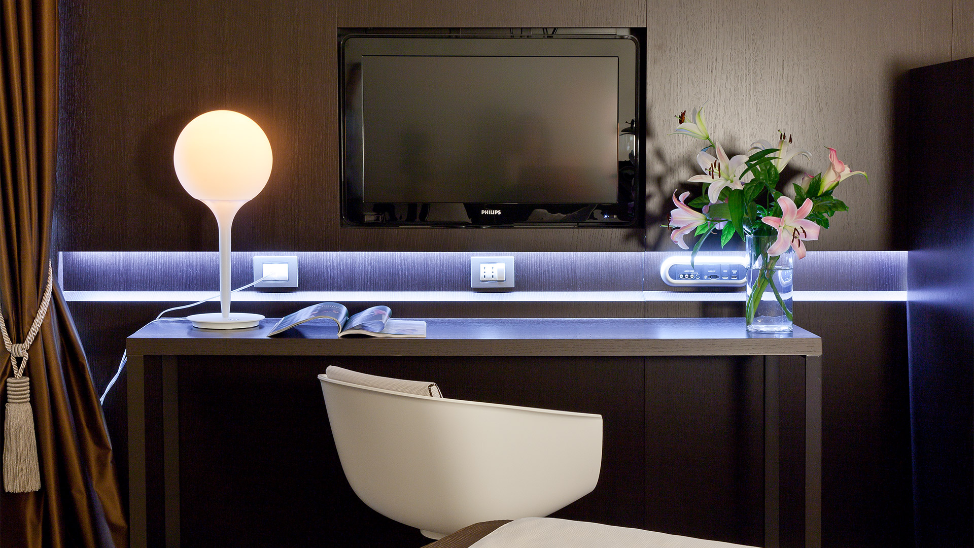 Lampada da tavolo Artemide Castore con diffusore sferico in vetro bianco su scrivania moderna d'hotel, con striscia LED blu