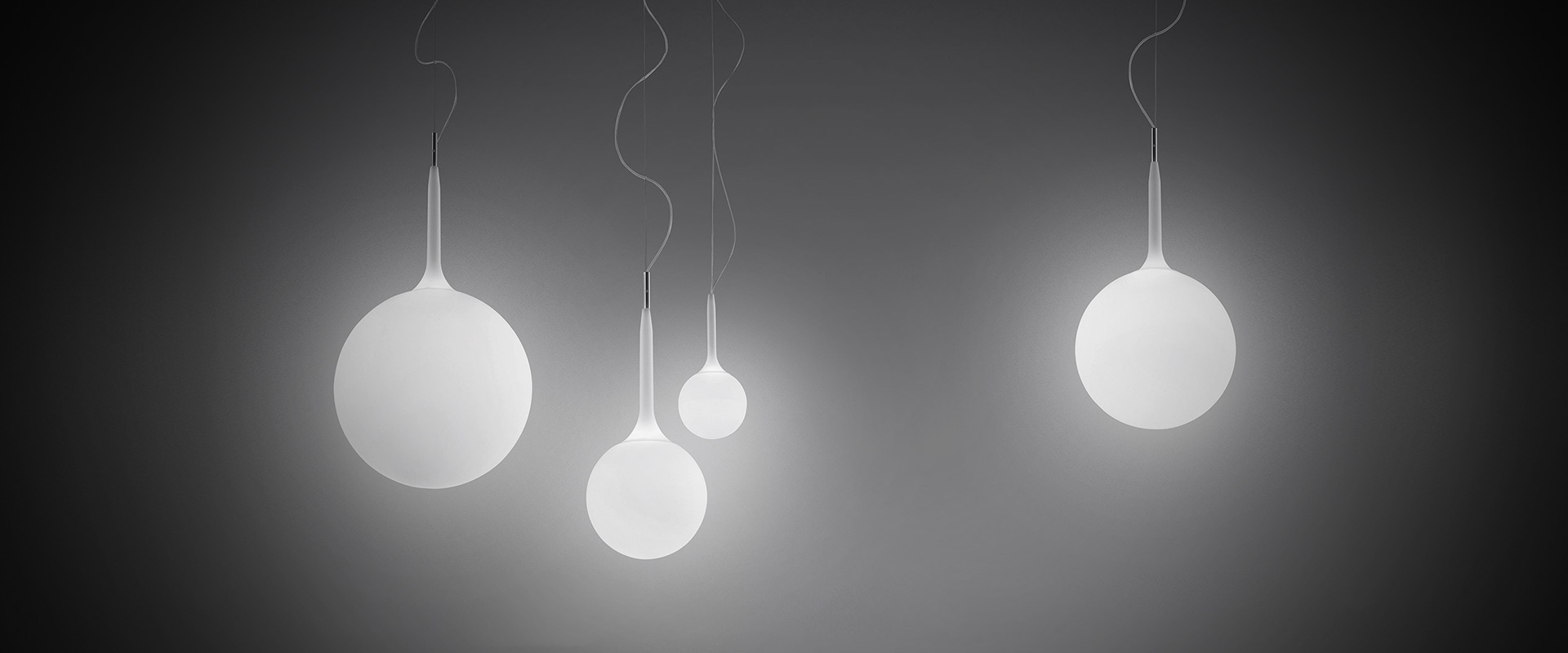 Castore Sospensione by Artemide: five white opal glass sphere pendant lamps in varying sizes hanging on thin cables against a dark background