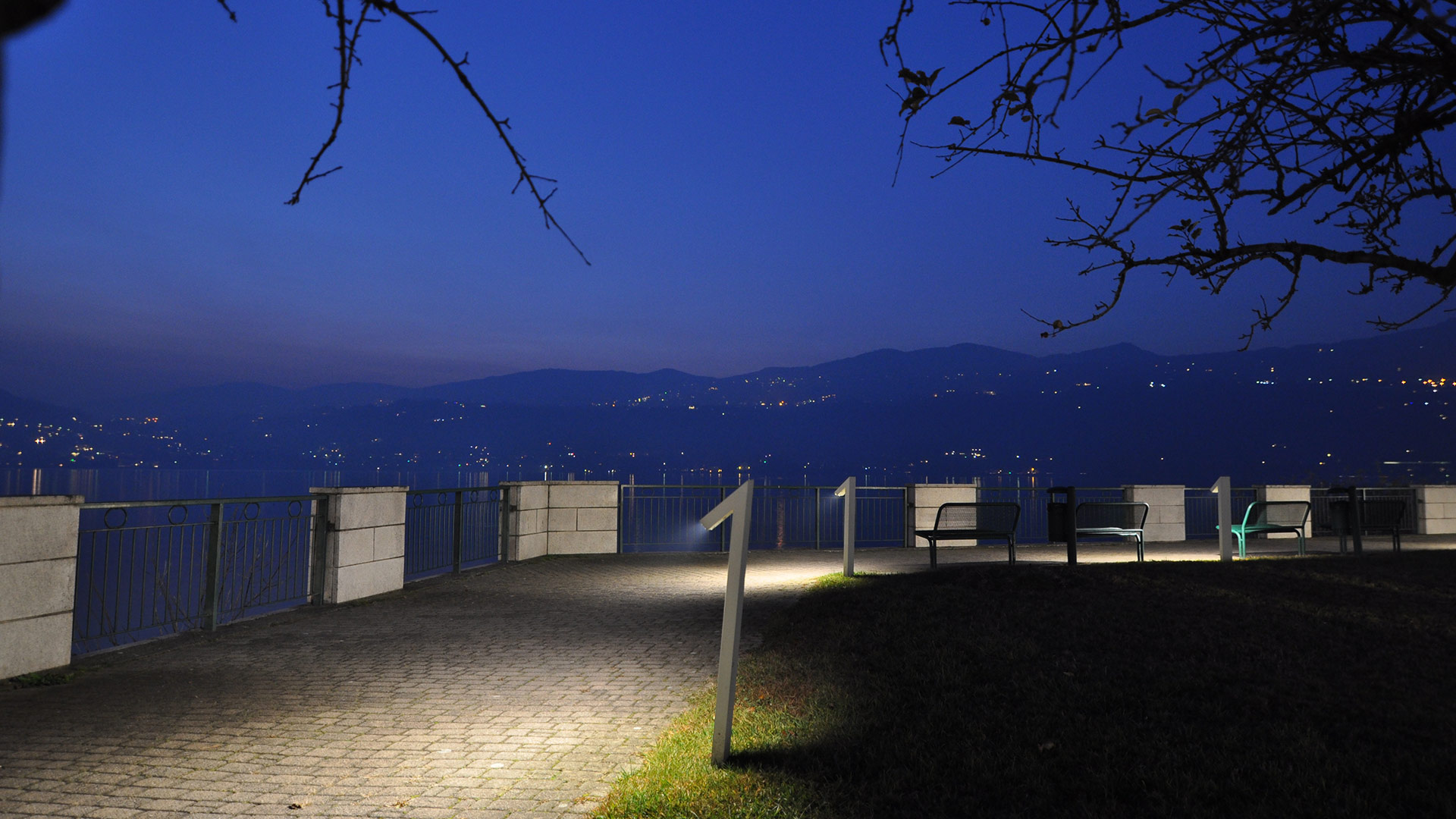 Vialetto da giardino di notte con faretti a picchetto Artemide Chilone che proiettano coni di luce calda sull'erba tra gli alberi