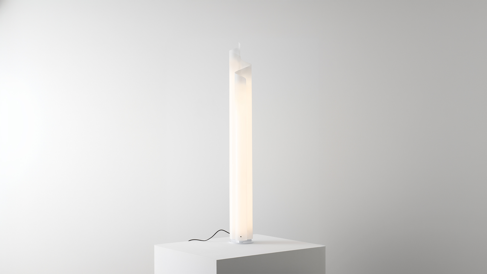 Artemide Chimera floor lamp: tall vertical luminous white column with asymmetric top diffuser, placed on a white pedestal