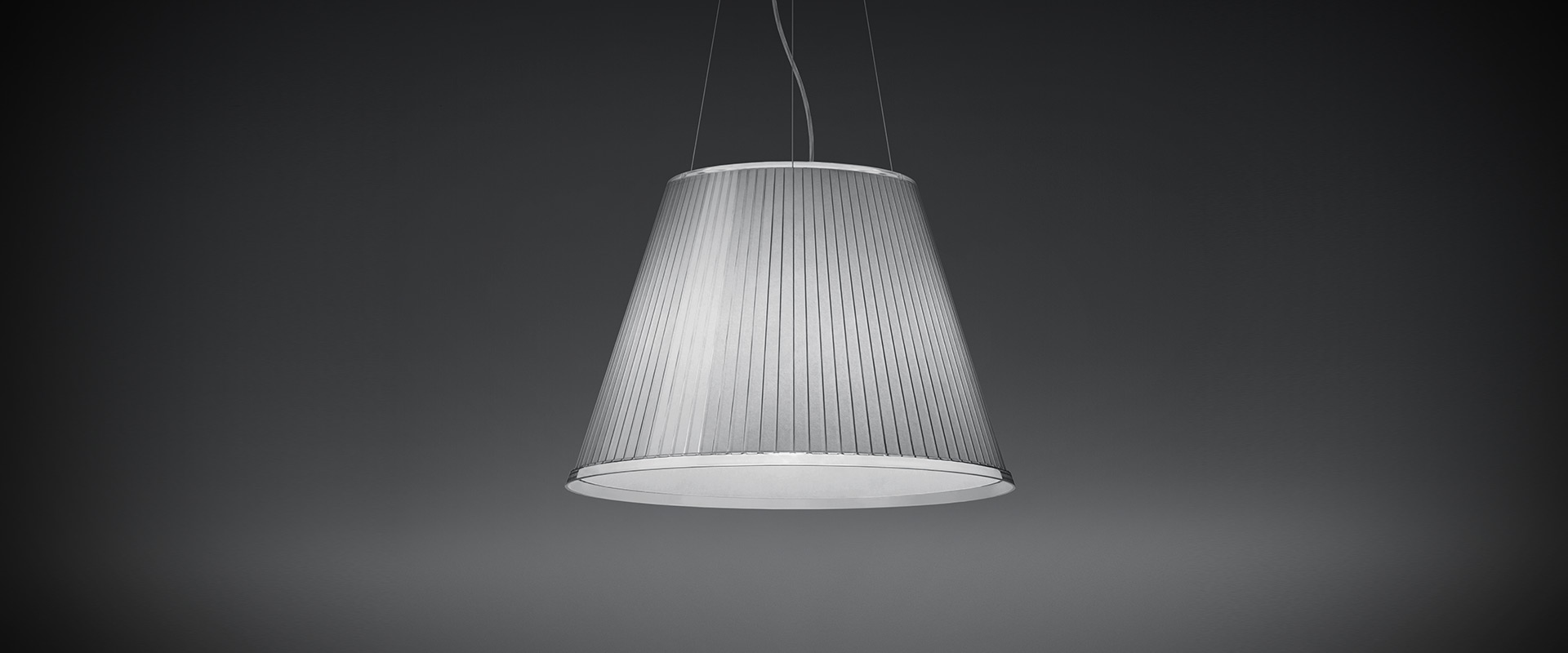 Lampada a sospensione Artemide Choose Mega con paralume in tessuto plissettato argento, forma conica, sospesa da sottili cavi su sfondo grigio