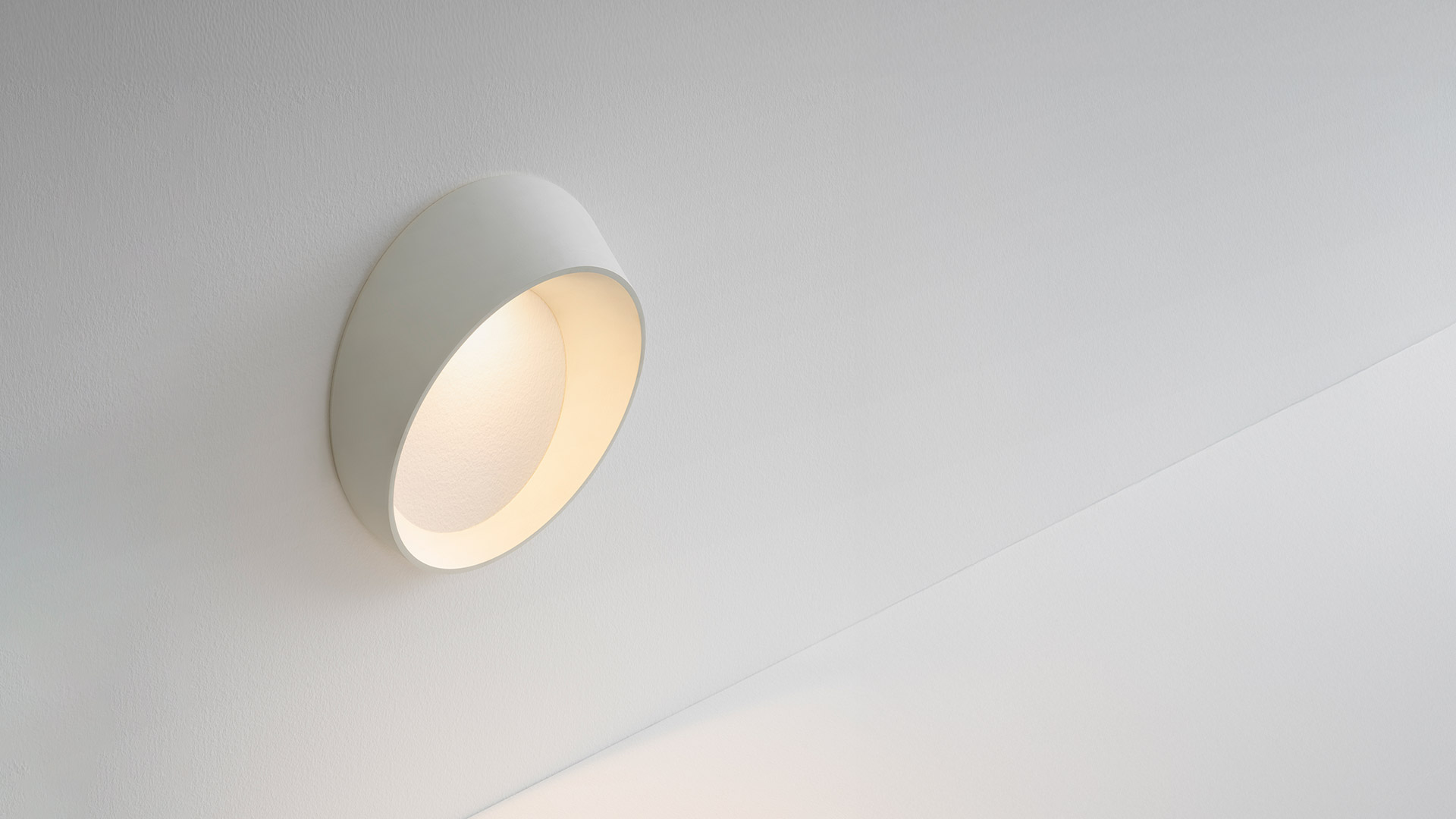 Applique da parete Artemide Cleomede: apparecchio circolare bianco a disco con coppa inclinata che emette luce calda diffusa