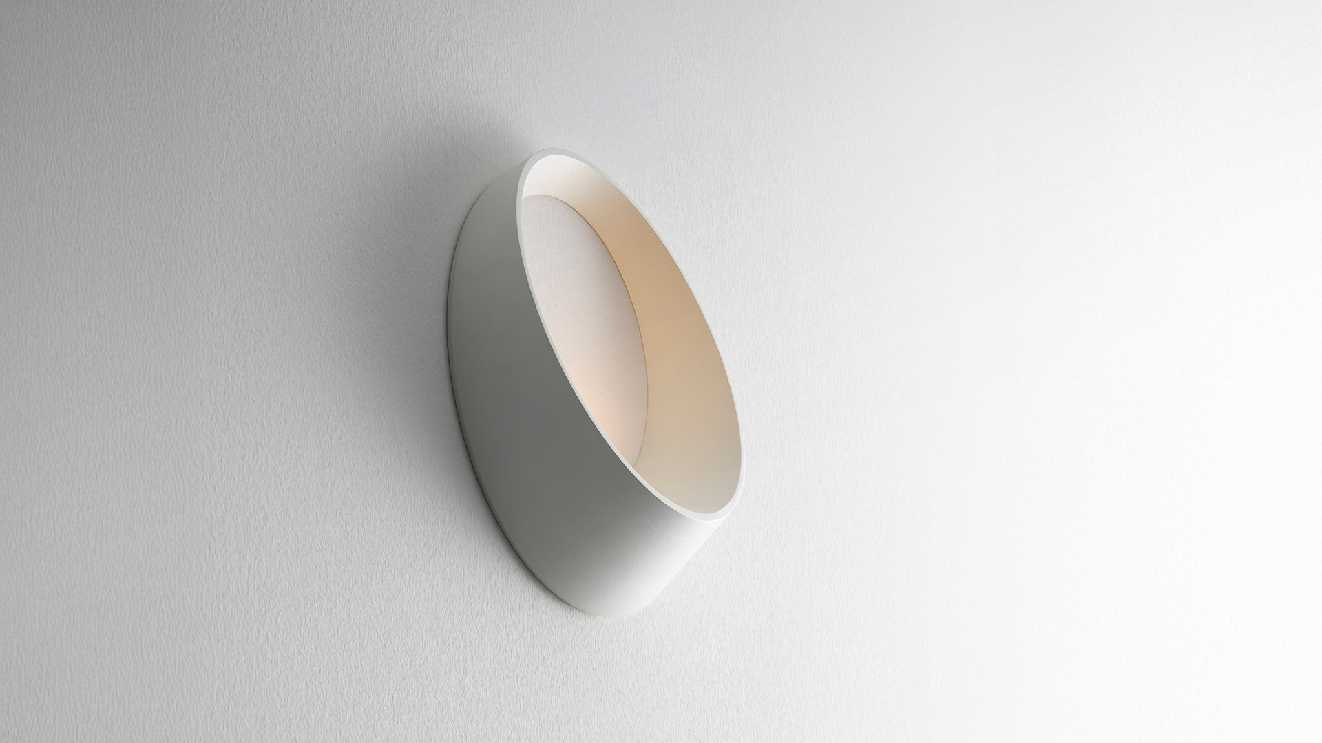 Lampada da parete Artemide Cleomede, design ad anello ovale bianco con piccola luce LED, montata su parete gialla testurizzata vicino a una scala