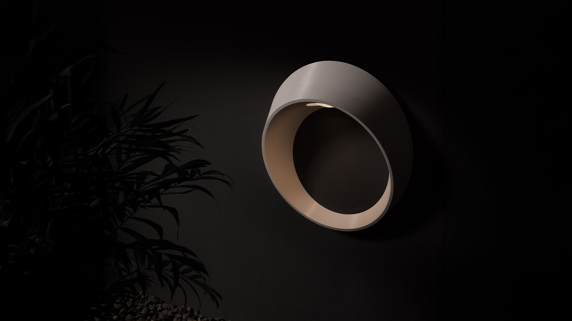 Lampada da parete Artemide Cleomede: applique circolare bronzo scuro che emette luce calda verso il basso da una piccola apertura, montata su parete scura