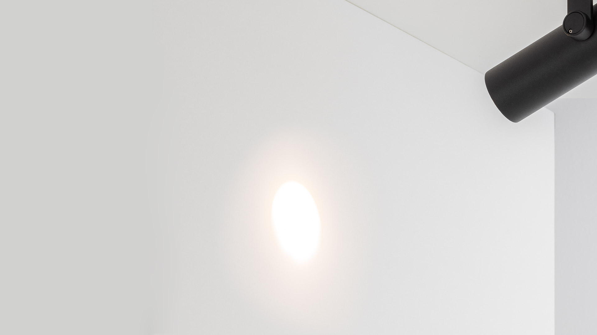 Artemide Coherence track spotlight in matte black, cylindrical body with warm LED source, adjustable mounting bracket