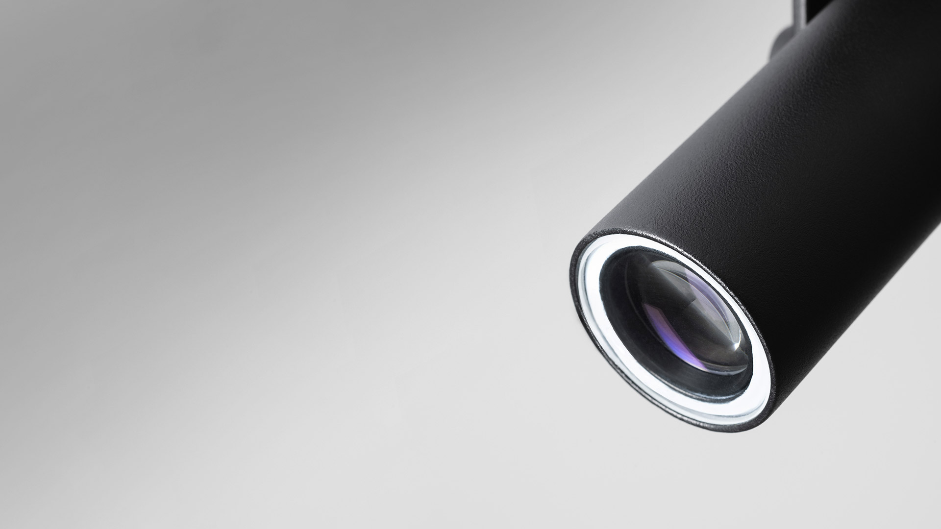 Black cylindrical Artemide Coherence track spotlight mounted on ceiling, projecting a warm white oval light beam on a white wall