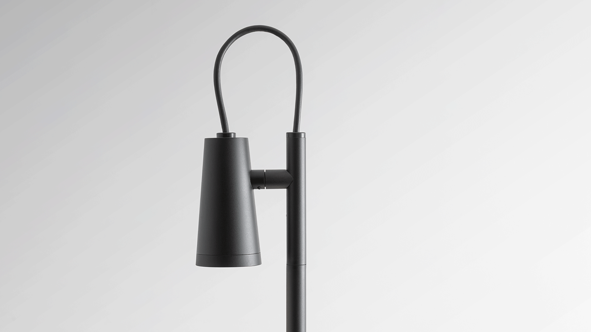 Lampada da esterno Artemide Conus su paletto in nero, con testa cilindrica orientabile, installata in un vialetto tra erba spontanea