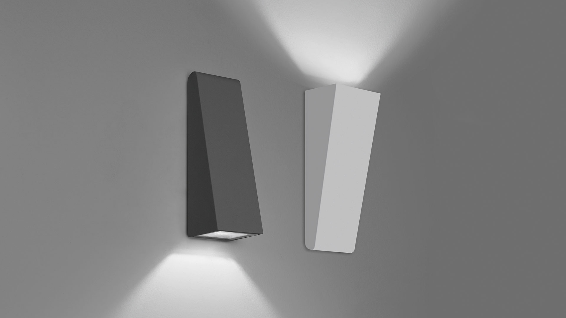 Due applique da parete Artemide Cuneo scure montate su un muro di pietra, che proiettano fasci di luce calda verso il basso, circondati da rigogliosa vegetazione verde di notte