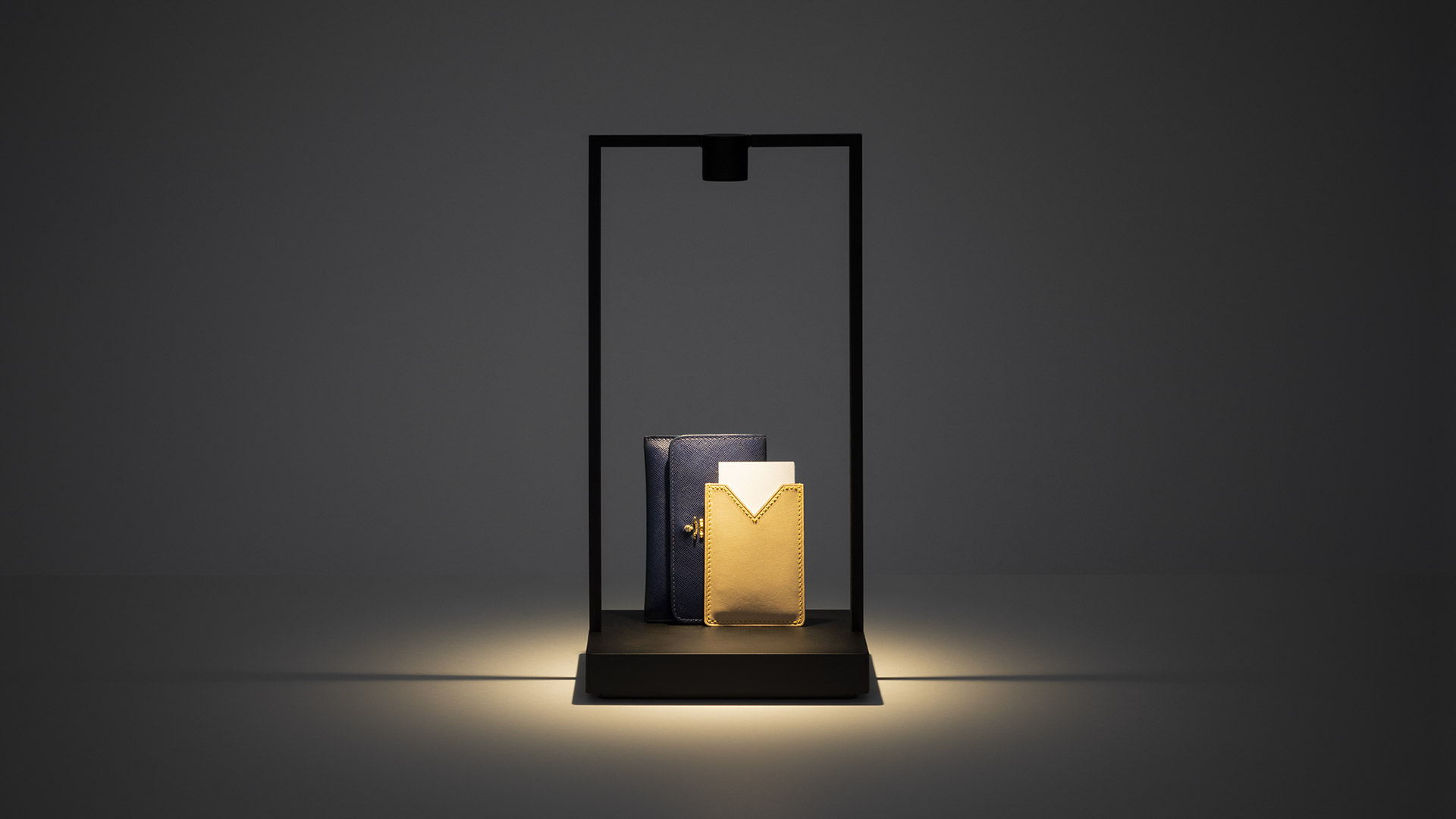 Tre lampade da tavolo Artemide Curiosity con strutture geometriche nere su superficie bianca, accanto a un'opera d'arte astratta colorata sulla parete