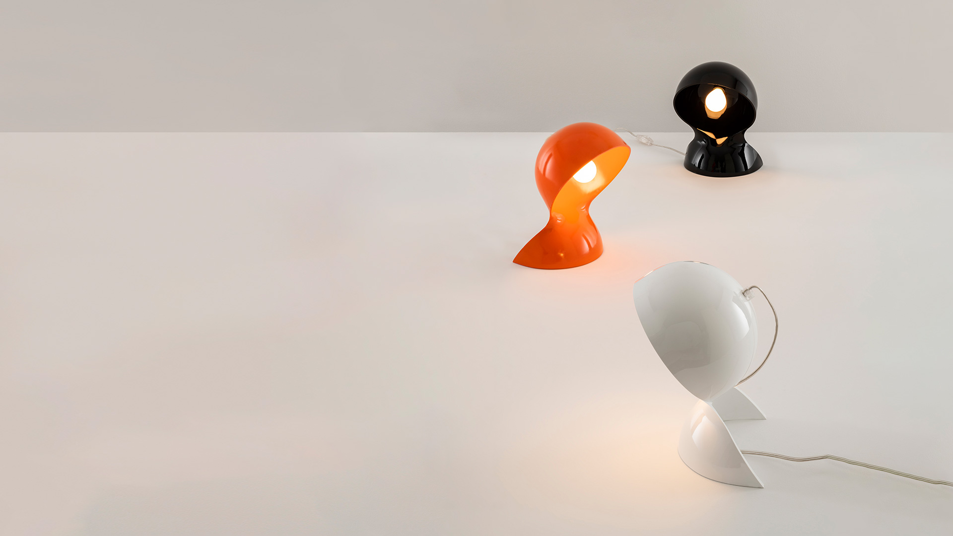 Lampada da tavolo Artemide Dalù arancione, esposta su un piedistallo a gradini rosso davanti a tende di velluto rosso intenso su un palcoscenico teatrale
