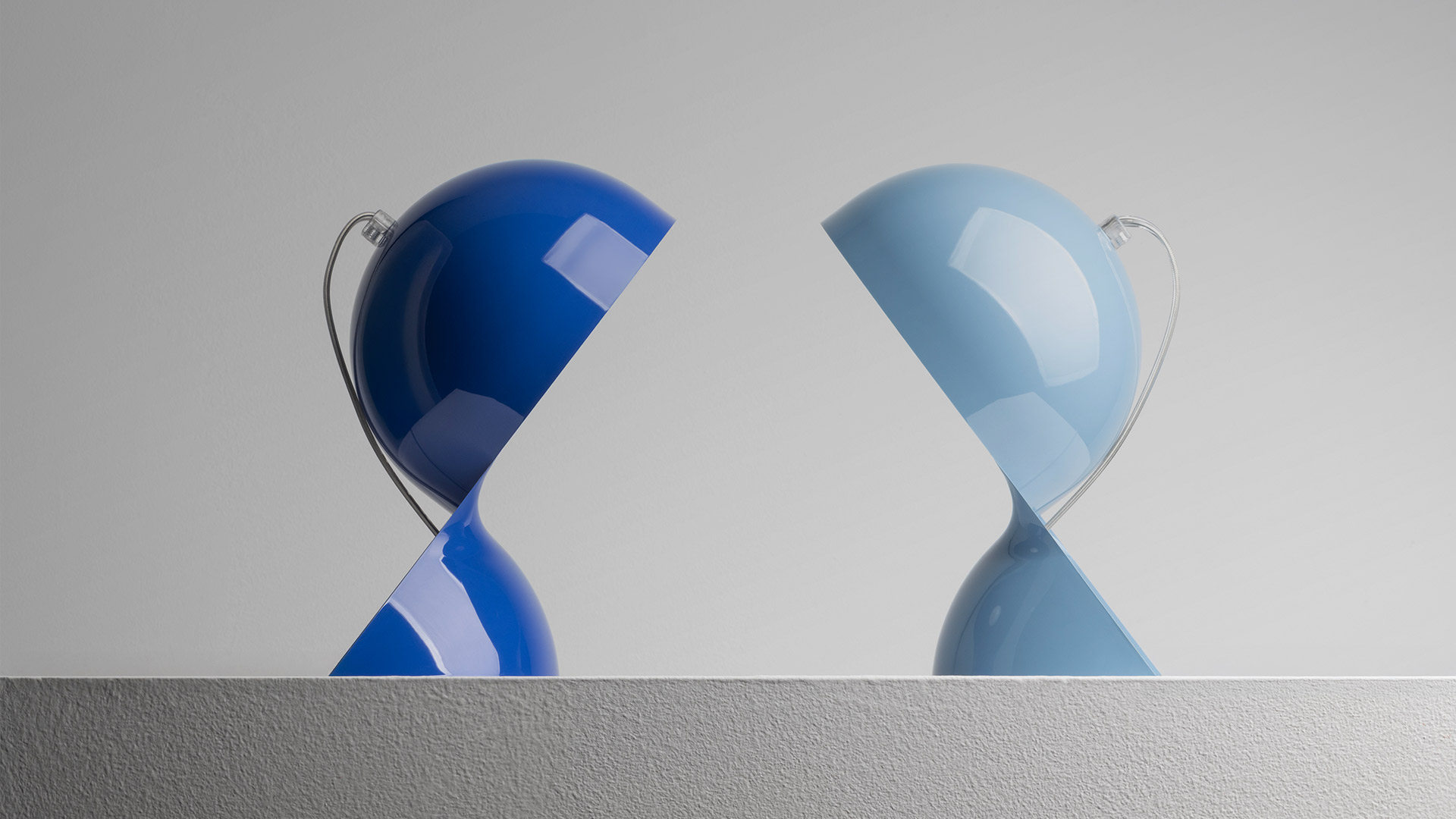 Due lampade da tavolo Artemide Dalù affrontate: sinistra blu scuro, destra azzurro chiaro, entrambe con paralume sferico lucido inclinato verso il basso