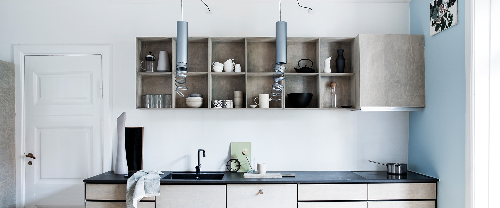 Modern kitchen with two Artemide Decomposé Light pendant lamps in grey, hanging above a minimalist counter with open shelving.