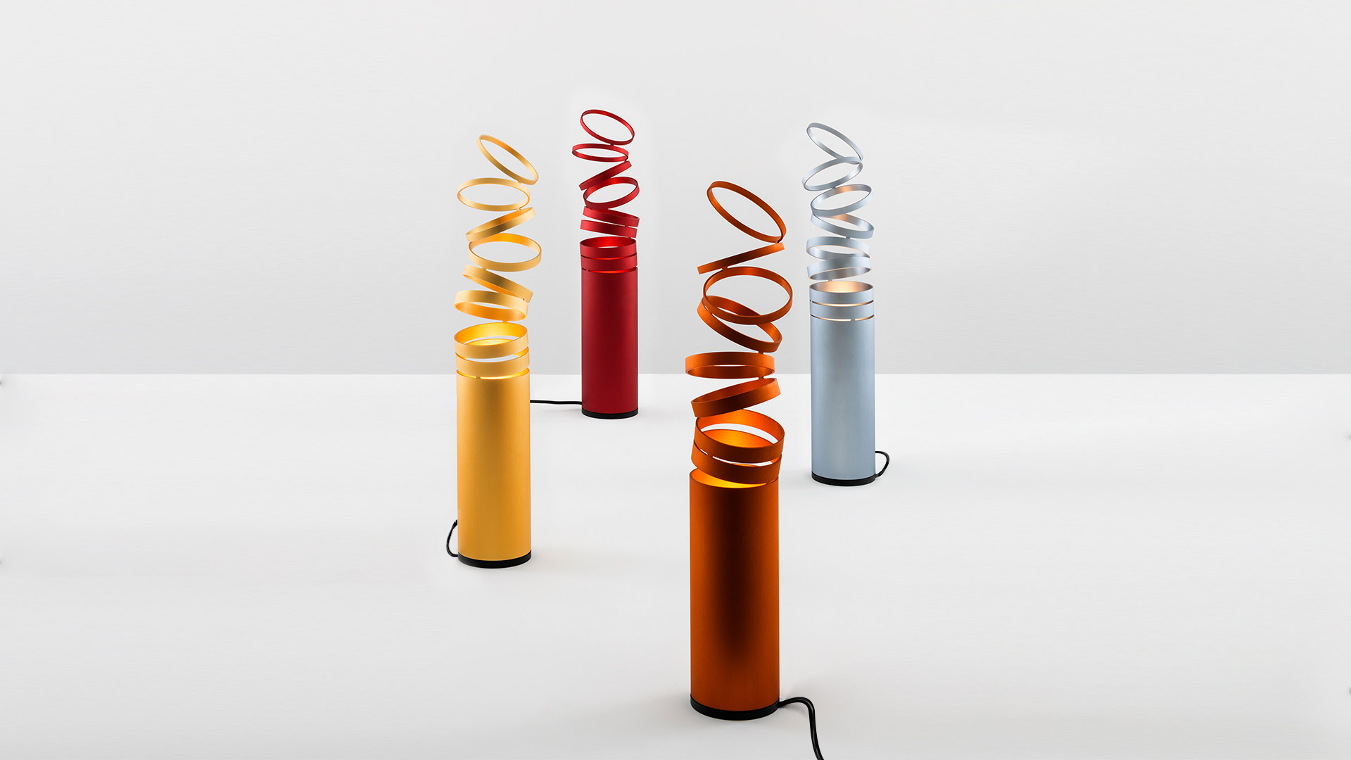 Quattro lampade da terra Artemide Decomposé Light Tavolo con basi cilindriche e paralumi a nastro spiralato in giallo, rosso, arancione e grigio