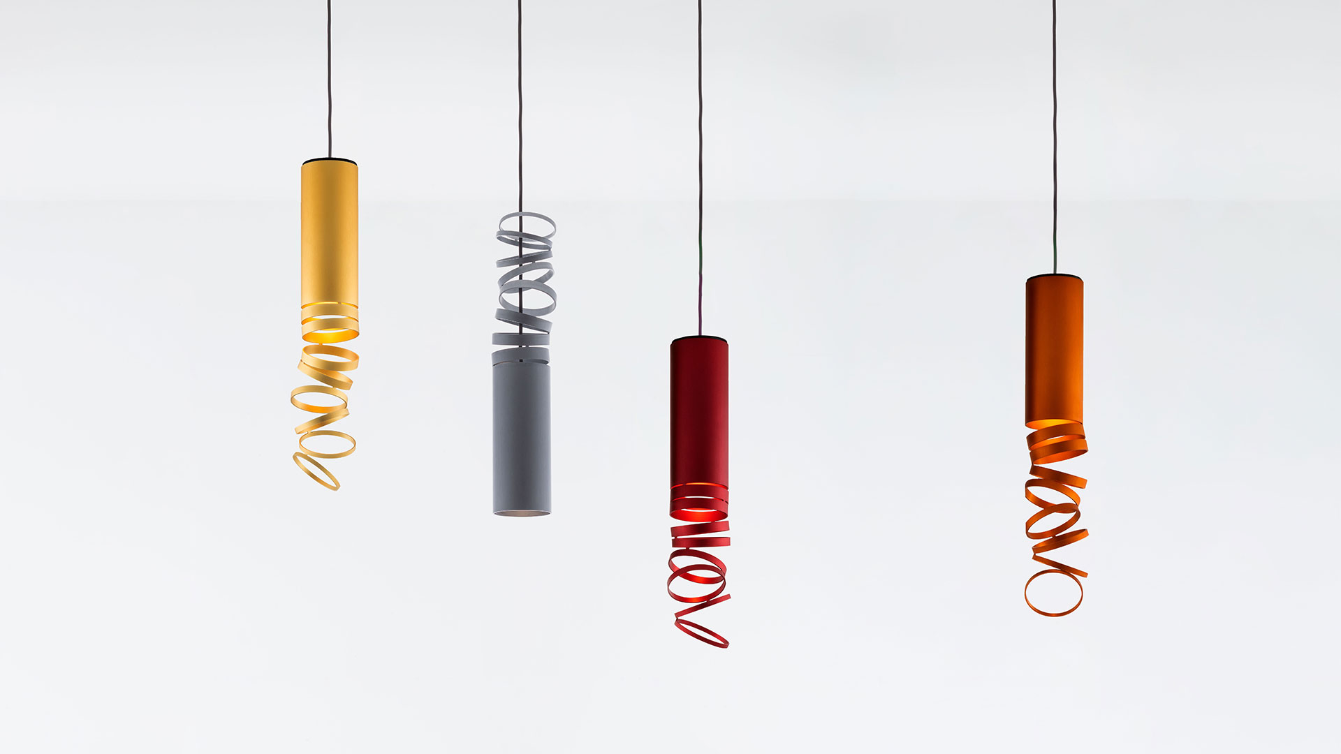 Four Artemide Decomposé Light pendant lamps in yellow, grey, red, and orange, each with a cylindrical body and spiral ribbon diffuser
